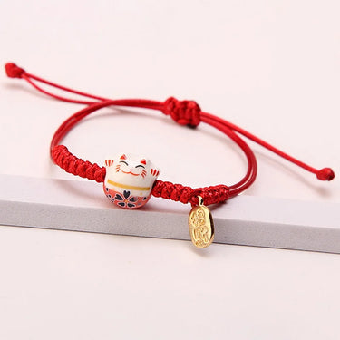 KittyNook Cat Co.'s Enchanting Lucky Cat Charm Bracelet features a red braid and gold pendant with Maneki-neko charm.